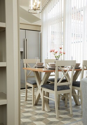 Un coin repas avec une table et des chaises en bois, un vase rempli de fleurs et une vue dégagée sur l’extérieur grâce à de grandes fenêtres.