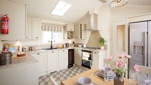 Una cocina moderna con armarios blancos, una estufa a gas y un horno empotrado. Hay una zona de comedor con una mesa dispuesta para dos personas, y un refrigerador con dispensador de agua.