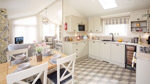 Una cocina moderna con armarios blancos, un comedor con una mesa dispuesta para cuatro personas y una sala de estar con sofá y televisor.