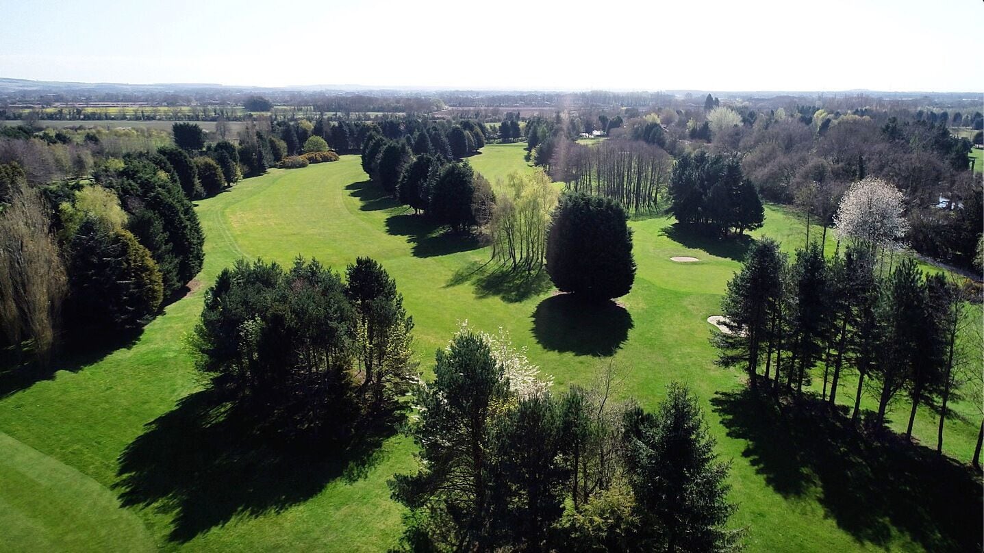 An aerial view of a golf course with multiple fairways, sand bunkers, and clusters of trees.