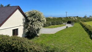 A house with a white exterior and a dark roof, surrounded by a well-maintained lawn and flowering bushes. - Ty Efail Cottage, Mountain Views & Secure Garden (Beaumaris)