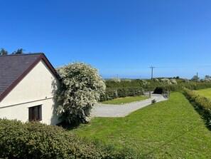 A house with a white exterior and a dark roof, surrounded by a well-maintained lawn and flowering bushes.