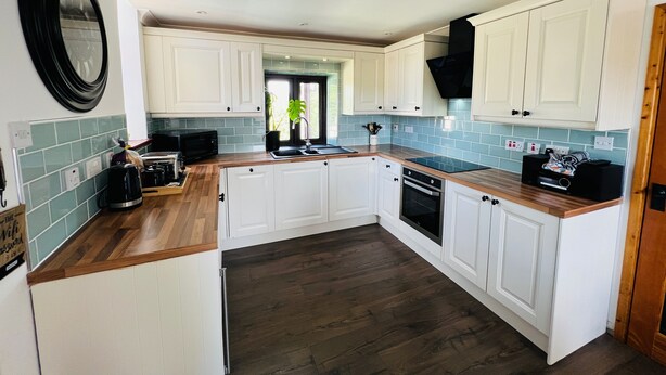 A modern kitchen with white cabinets, a wooden countertop, and a black range hood. - Ty Efail Cottage, Mountain Views & Secure Garden (Beaumaris)