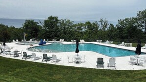 Una piscina con tumbonas y sombrillas, rodeada de césped y árboles.