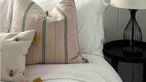 Ein ordentlich eingerichtetes Schlafzimmer mit einem Bett, Kissen, einem gerahmten Gemälde und einem Nachttisch mit einer Lampe.