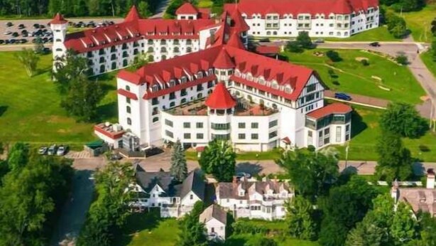 Ein großes, mehrstöckiges Hotel mit roten Dächern, umgeben von üppiger Vegetation und einem See.