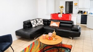 Uma sala moderna com um sofá seccional preto, uma mesa de centro redonda e um tapete colorido.