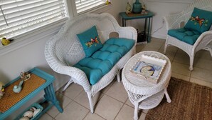 A cozy room with wicker furniture, including a sofa and chairs, a small table, and a window with blinds. - Sunkissed Cottage (Gulfport)