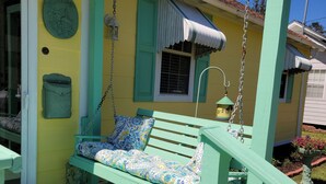 A porch with a swing seat, a welcome sign, and a bird feeder. - Sunkissed Cottage (Gulfport)