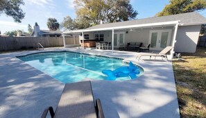 A backyard with a swimming pool, a covered patio area, and a wooden deck.