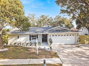 A single-story house with a front garage, a small porch, and a well-maintained lawn. - Luxe by the Bay - A TOGAR Family Vacation Rental (Largo)