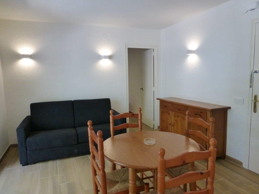 Una stanza con un tavolo rotondo in legno, quattro sedie, un divano scuro e un armadietto in legno.