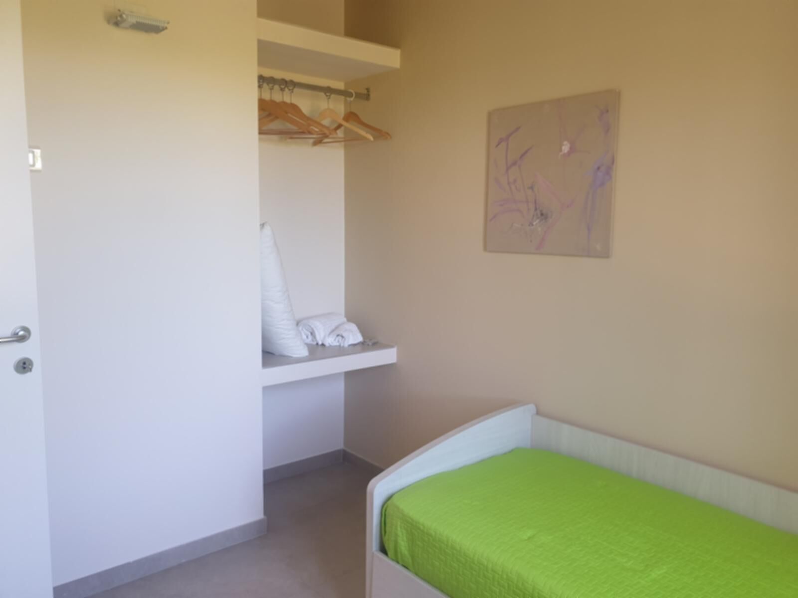 Une chambre à coucher avec un lit, une armoire où sont suspendus des vêtements, et un mur orné d’un tableau.