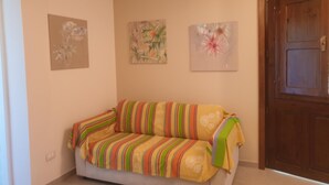 Une pièce avec un canapé, trois œuvres d’art encadrées accrochées au mur et une porte en bois.