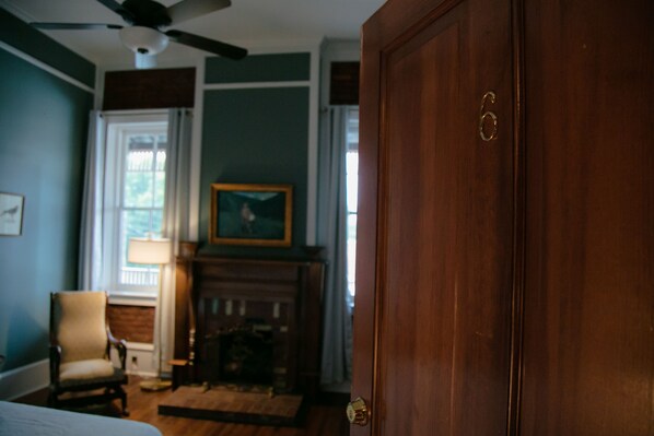 A room with a wooden door, a chair, a fireplace, and a painting on the wall. - The Grand Hotel (Hogansville)