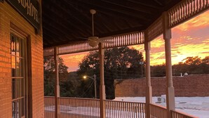 A covered porch with a ceiling fan, a brick wall with a sign reading "GRAND HOTEL", and a view of the sunset over a snowy landscape. - The Grand Hotel (Hogansville)