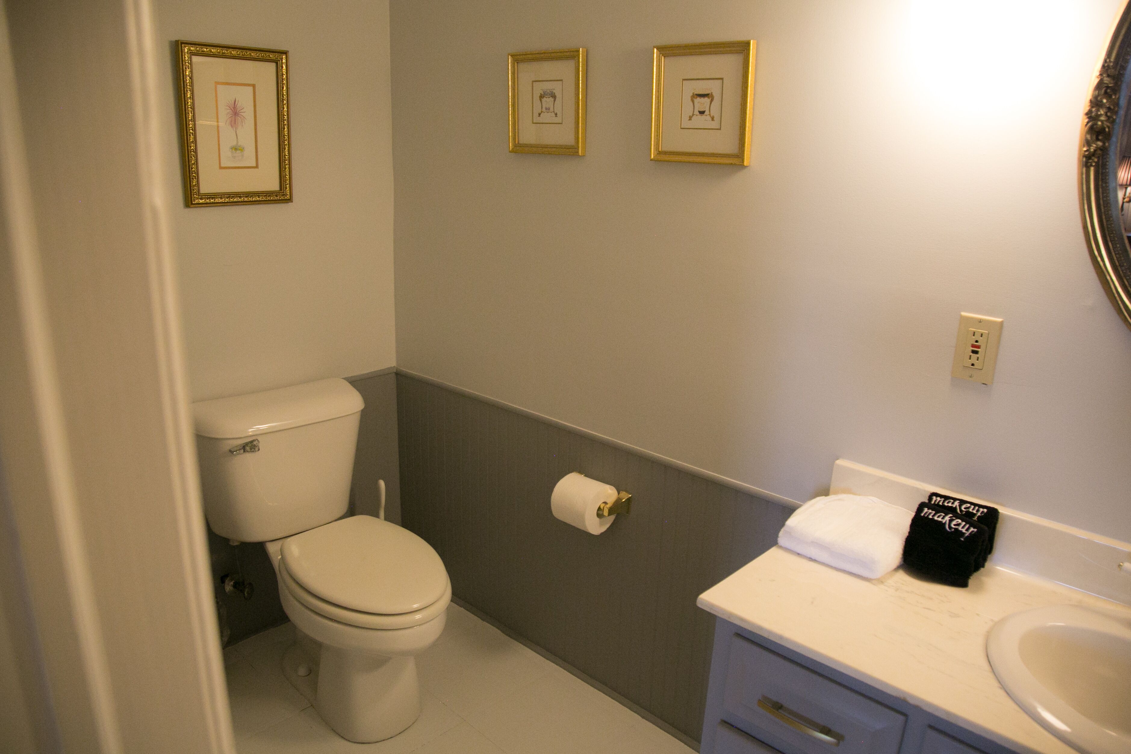 Un baño con inodoro, lavamanos y fotografías enmarcadas en la pared.