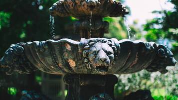 A multi-tiered fountain with lion sculptures at its base, set in a garden with trees in the background.