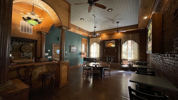 A spacious room with wooden floors, a bar area, and a fireplace. - The Grand Hotel (Hogansville)