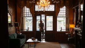 A cozy room with a green sofa, a small table, and a chandelier. - The Grand Hotel (Hogansville)