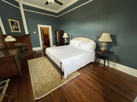Un dormitorio con una cama, cómoda de madera, dos mesitas de noche con lámparas, una puerta y una alfombra estampada.