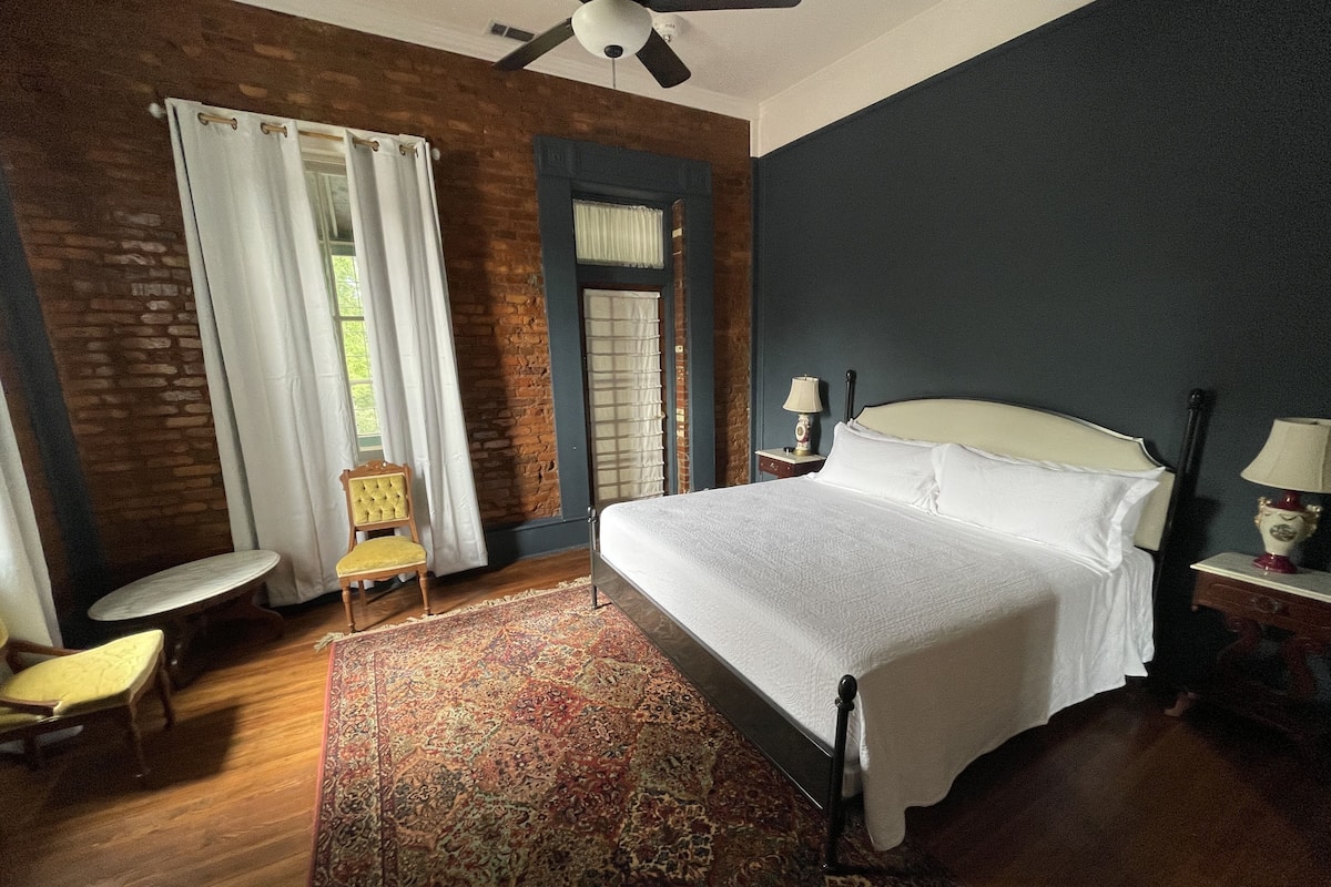 Une chambre à coucher avec un grand lit, un ventilateur de plafond, une chaise, une table de chevet et un tapis.