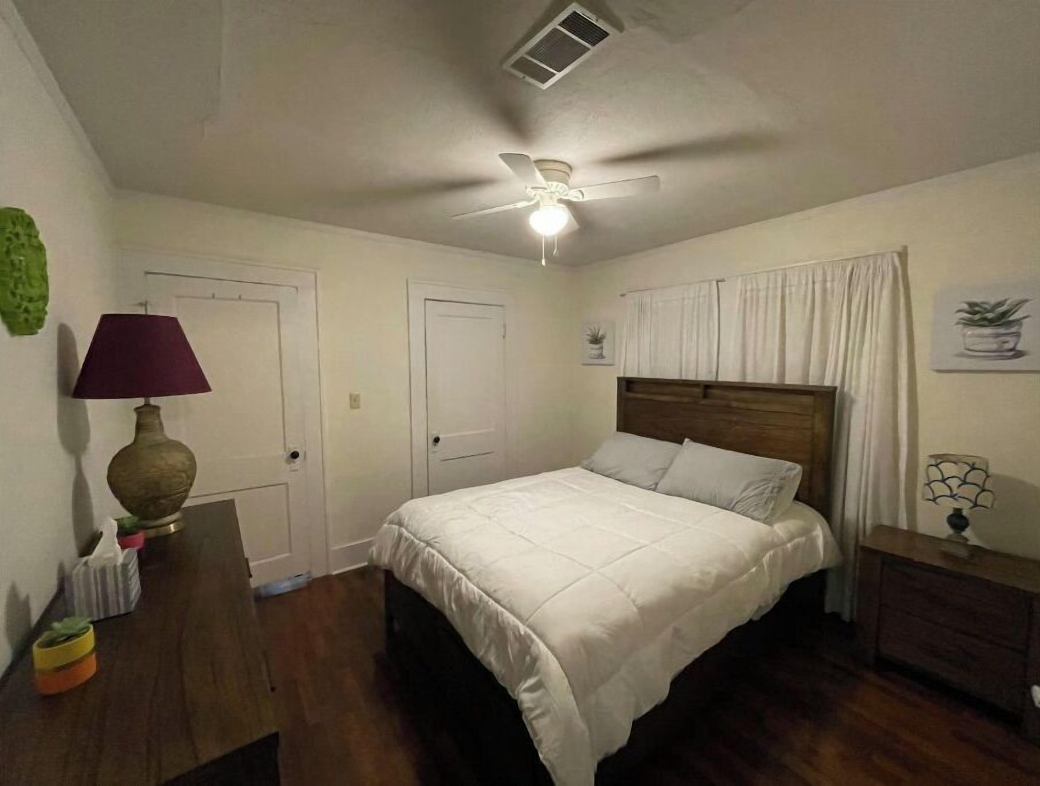 A bedroom with a bed, a ceiling fan, a nightstand, a lamp, and a dresser.