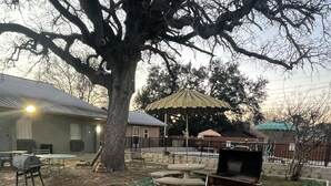 Un jardin avec un barbecue, du mobilier d’extérieur et un grand arbre.