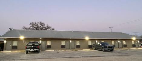 A motel with a row of rooms, a parking lot, and two parked vehicles.