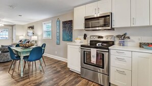 Una cocina moderna con gabinetes blancos, electrodomésticos de acero inoxidable y un comedor con sillas azules.