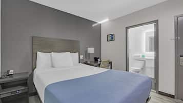 Ein Hotelzimmer mit einem großen Bett, Nachttisch, Lampe und Blick ins Bad.