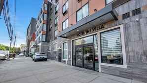 Un hotel moderno con fachada de vidrio, una entrada visible y un área de estacionamiento.