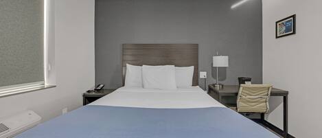 A hotel room with a large bed, a bedside table with a lamp, a chair, and a window.