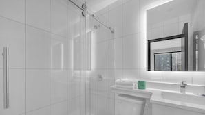 Un baño moderno con ducha de vidrio, inodoro y lavamanos con espejo.