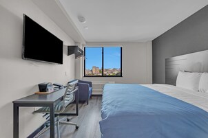 Ein Hotelzimmer mit Bett, Schreibtisch, Sessel, Fernseher und Fenster mit Blick auf die Stadt.