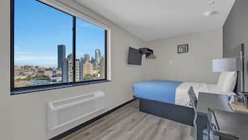 A modern hotel room with a large window, a bed, a desk, and a city view.