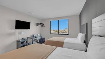 Habitación de hotel con dos camas, televisión, escritorio y ventana con vista a la ciudad.