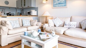 A modern living room with a sofa set, a coffee table with books and a teapot, a kitchen area with a microwave and kettle, and a painting on the wall. - Slipway 12 (Wadebridge)