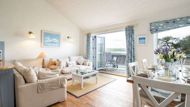 A cozy living room with a sofa, coffee table, and a dining area with a table set for two. - Slipway 12 (Wadebridge)