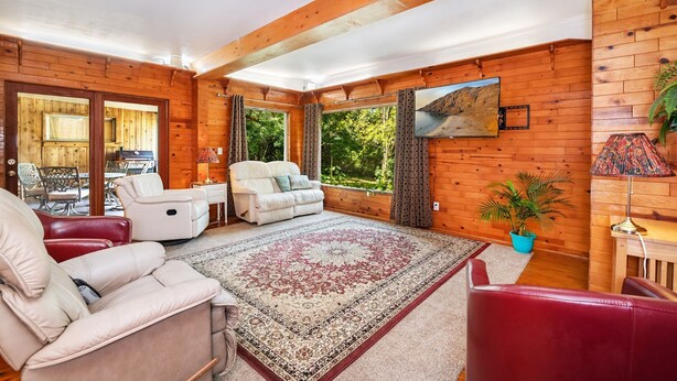 Una habitación acogedora con paredes de madera, un ventanal grande, un sofá, una silla y una mesa con sillas.