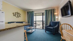 A compact hotel room with a kitchenette, a sofa, a chair, a small table, and a TV mounted on the wall. - Sea Shack! (Galveston)