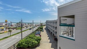 A hotel with a row of balconies, a parking lot, and a view of the beach and ocean. - Sea Shack! (Galveston)
