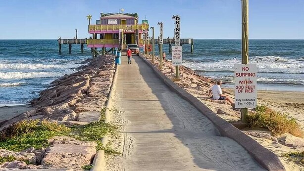 A pier with a building at the end, a sign prohibiting surfing within 300 feet of the pier, and a clear blue sky. - Sea Shack! (Galveston)