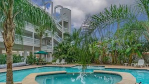 A pool area with a stone border, lounge chairs, and a palm tree. - Sea Shack! (Galveston)