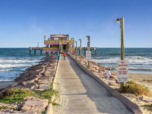 A pier with a building at the end, a sign prohibiting surfing within 300 feet of the pier, and a clear blue sky. - Sea Shack! (Galveston)