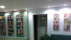 Una biblioteca con estanterías, un sofá verde y arte floral en la pared.