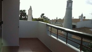 Un balcón con suelo de baldosas, barandilla y vista a edificios y una torre a lo lejos.