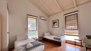 Een slaapkamer met twee bedden, een bureau en een raam met jaloezieën.