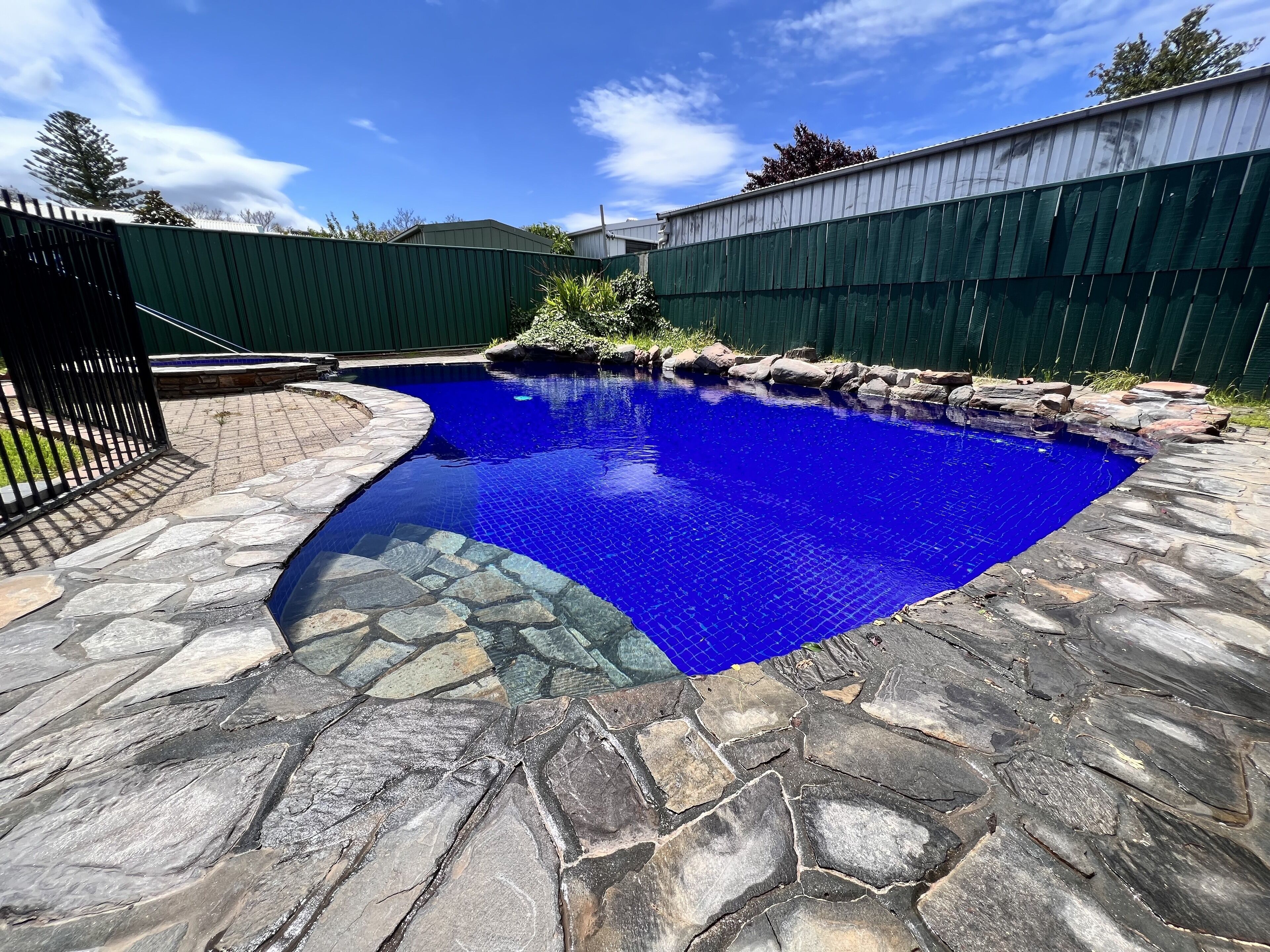 A swimming pool with a stone border and a metal fence.