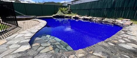A swimming pool with a stone border and a metal fence.